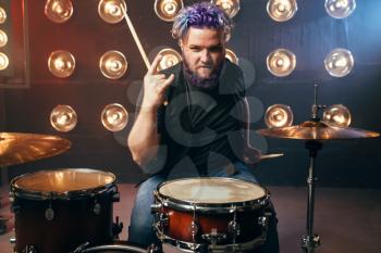 Bearded drummer with colorful hair, rock performer on the stage with lights, vintage style. Musical concert in night club