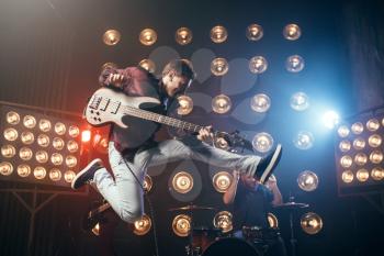 Guitarist plays on bas-guitar, snapshot in a jump, stage with lights on background. Rock band concert