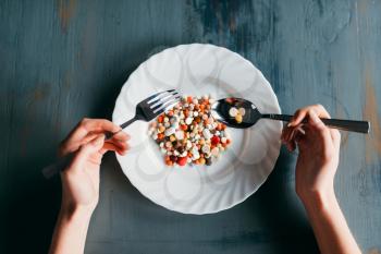 Female hands with spoon and fork, plate full of drugs, top view. Weight loss diet concept