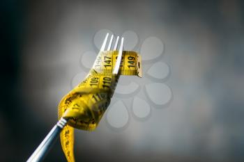 Measuring tape is wound on a fork closeup, nobody. Weight loss diet concept