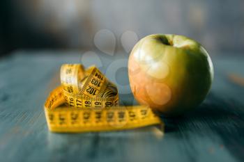 Apple and measuring tape on wooden table closeup. Weight loss diet concept, fat burning