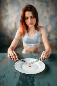 Unhappy young woman against plate with a tablet for weight loss. Fat or calories burning concept