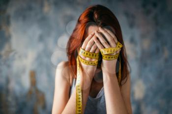Woman covers face with her hands tied with measuring tape. Fat or calories burning concept. Weight loss