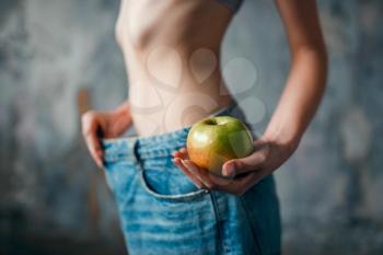 Woman with apple in hand tries on big size jeans, weight loss. Fat or calories burning concept, hard dieting