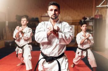 Martial arts karate fighters, master and his disciples in white kimono and black belts hone their skills, fight training in action, workout in gym