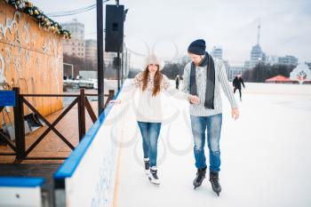 Love couple, man learn woman to skate on the rink. Winter skating on open air, active leisure, ice-skating