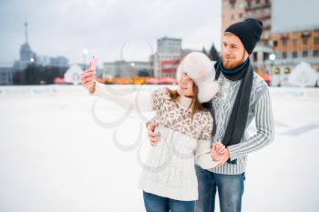Happy love couple makes selfie on skating rink. Winter ice-skating on open air, active leisure, man and woman skates together