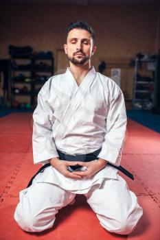 Martial arts, man in white kimono with black belt, meditating in gym