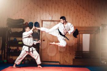 Martial arts karate masters in white kimono and black belts, karate practice in gym, kick in jump