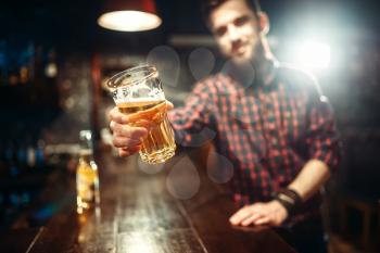 One bearded man holds glass of beer, guy at the bar counter. Male person leisure in pub