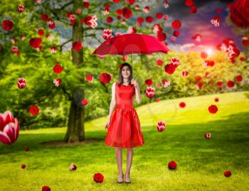 Happy woman in red dress with umbrella in green summer park. Female person with parasol in beautiful forest, flowers flying everywhere