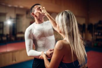 Female person makes pain in the eyes, self-defense workout with male personal trainer, gym interior on background. Woman on self defense training