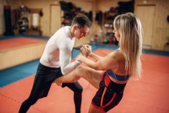 Female fighter hiding from a knife strike on self defense workout with male personal trainer, gym interior on background. Woman on training, self-defense practice