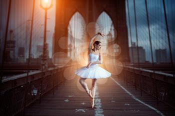 Ballet dancer in white dress dancing on the bridge in the evening. Graceful ballerina training in class