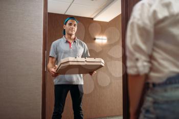 Pizza delivery boy with carton box in hands on the doorstep, delivering service. Courier from pizzeria and customer indoors