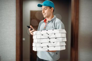 Pizza delivery boy in t-shirt and cap calls to customer, delivering service. Courier from pizzeria holds cardboard packages and phone