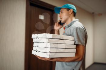 Pizza delivery man at the door calls to customer, delivering service. Courier from pizzeria holds carton boxes and talk by phone indoors