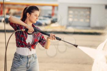 Young woman on self-service car wash. Outdoor vehicle washing at summer day. Female person with high pressure water gun