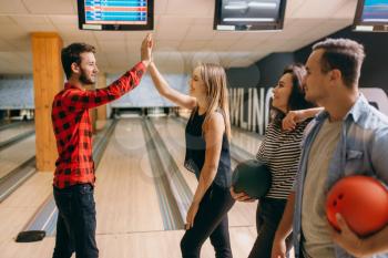 Bowler throws ball on lane and makes strike shot. Bowling alley team congratulates each other, successful throwing. Men and women playing the game in club, active leisure