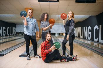 Bowling team poses on lane with balls on hands. Players before competition. Friends playing classical tenpin game in club, active leisure