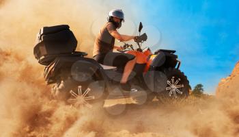 Atv in dust clouds, sand quarry on background. Male driver in helmet on quad bike in sandpit
