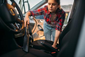Woman cleans car interior with vacuum cleaner, carwash. Lady with hoover on self-service automobile washing. Outdoor vehicle cleaning at summer day 