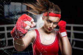 Female boxer in red gloves and sportswear training in gym, crushing blow, boxing workout