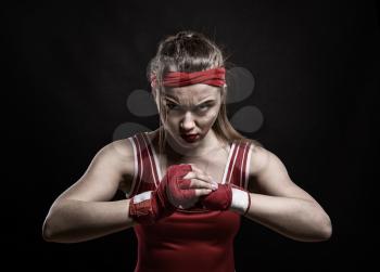 Female kickboxer in red gloves and sportswear, black background. Woman on boxing workout