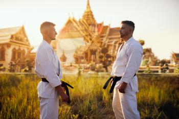 Black belt karate fighters in white kimono against ancient temple on sunset. Martial art training outdoor. Photo manipulation with background