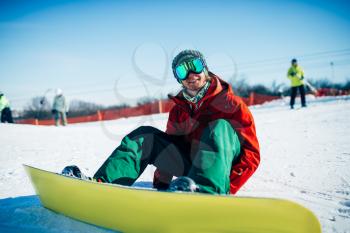 Snowboarder in glasses sitting on snowy slope. Winter extreme sport, active lifestyle. Snowboarding in mountains