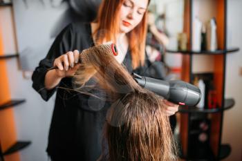 Hairdresser drying hair with a dryer, female hairdress in hairdressing salon. Hairstyle making in beauty studio