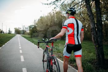 Cyclist in helmet and sportswear rides on bicycle, back view. Workout on bike path, cycling