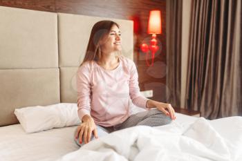 Young woman sitting in bed in yoga pose, morning relaxation, bedroom interoir on background