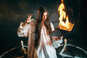Young woman in white shirt sitting in the center of burning pentagram circle and reads spellbook, gark magic ritual