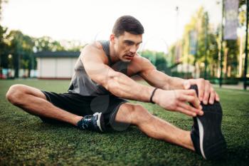 Male athlete on outdoor fitness workout. Sportsman sits on grass and doing stretching exercise