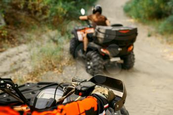 Two quad bike riders in helmets travels in forest, front view. Riding on atv, extreme sport and travelling, quadbike adventure