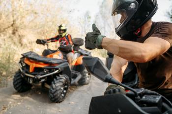 ATV rider in helmet showing thumbs up to his partner, offroad trip in the forest. Riding on quad bike, extreme sport and travelling, quadbike adventure