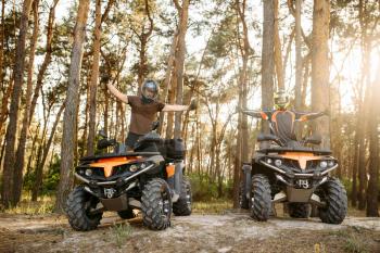 Two atv riders in helmets happily raise their hands up after extreme offroad riding, front view from the ground. Freeriding on quad bike, quadbike summer adventure