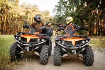 Two atv riders in helmets hits fists for good luck before dangerous extreme offroad riding, front view, summer forest on background. Freeriding on quad bike, quadbike adventure