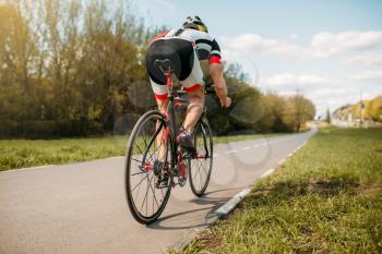 Cyclist in helmet and sportswear rides on bicycle, side view. Workout on bike path, cycling