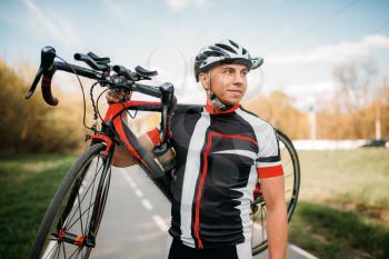 Bycyclist in helmet and sportswear keeps the bike on shoulder after biking on asphalt road
