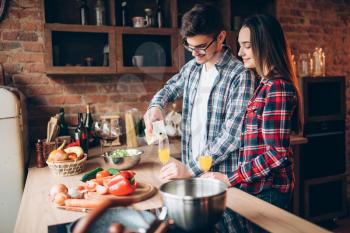 Husband pours fresh fruit juice in a glass, family cooking romantic dinner together.  Couple prepares healthy food dinner together. Vegetable salad preparation on the kitchen