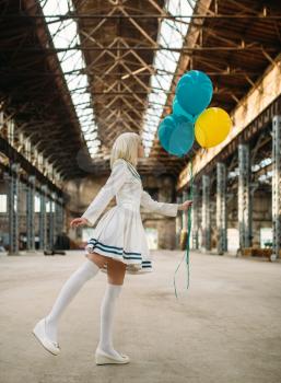 Pretty anime style blonde girl poses with colorful air balloons. Cosplay fashion, asian culture, doll in dress, cute woman with makeup in the factory shop