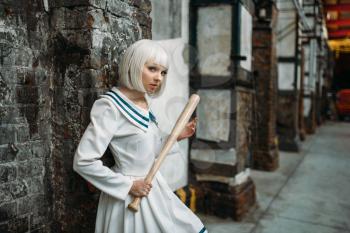 Anime style girl with baseball bat, lolita. Cosplay fashion, asian culture, manga doll in uniform, cute woman with makeup in abandoned factory shop
