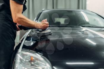 Male person with polishing machine cleans car. Auto detailing on carwash station, restore the paint of vehicle