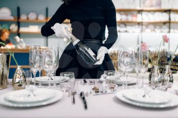 Waitress with a bottle of champagne, table setting. Serving service, festive dinner decoration, holiday dinnerware