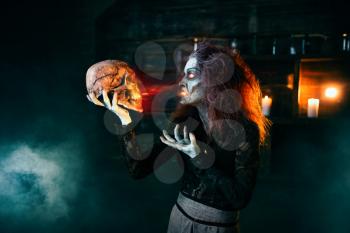Scary witch holds human skull and reads the spell, dark powers of witchcraft, spiritual seance. Female foreteller calls the spirits, terrible future teller