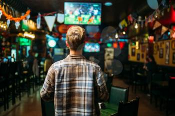 Football fan watching the match of the favorite team in sports bar, back view. Tv broadcasting of the game in pub
