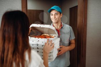 Delivery man shows fresh and hot pizza to female customer at the door, delivering service. Deliver from pizzeria and woman near the entrance to the apartment