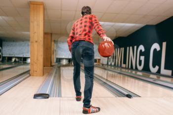 Male bowler throws ball on lane, back view. Bowling alley player playing tenpin game in club, active leisure